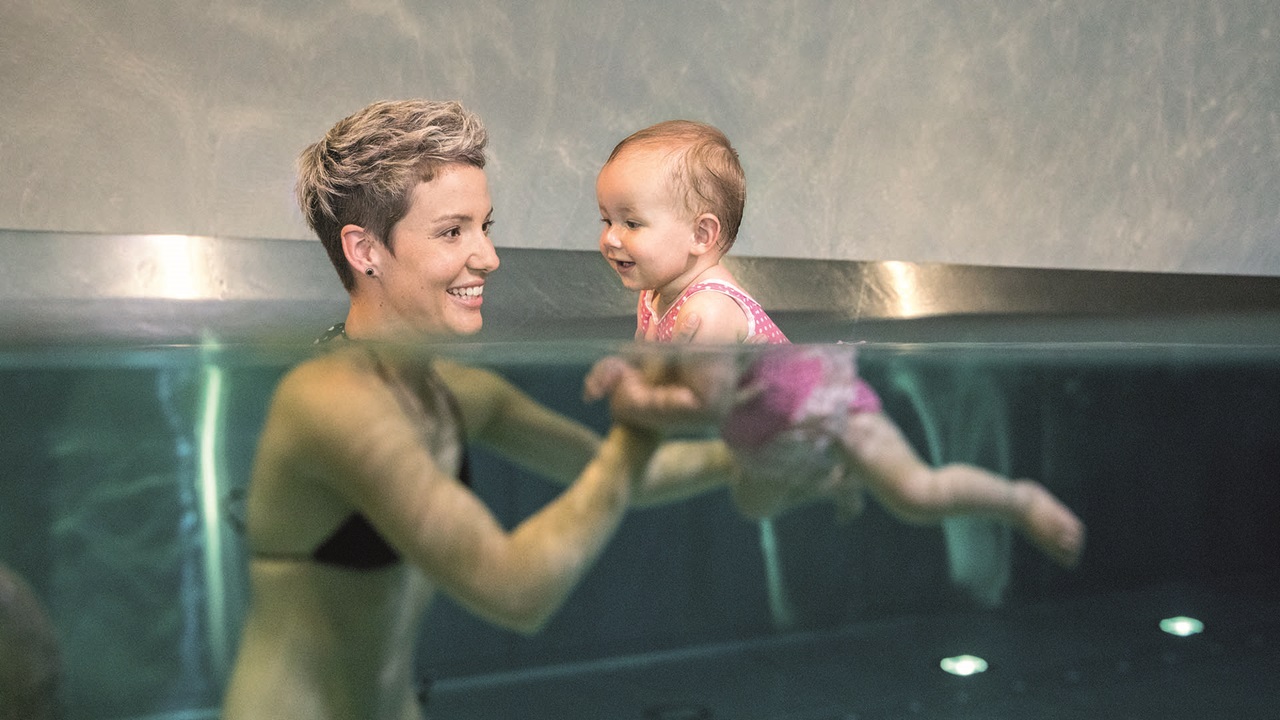 Femme avec son bébé dans l'eau pendant le cours de natation pour bébé First Flow Minis à Bernaqua.