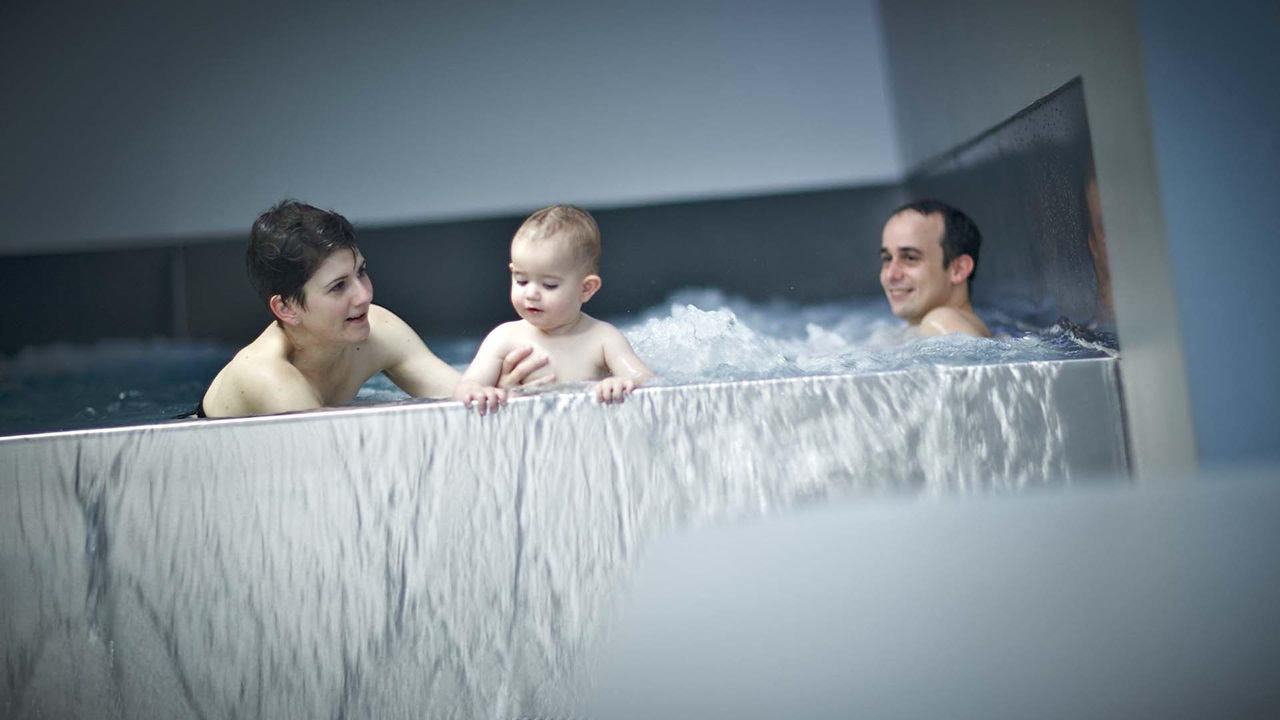 Une famille avec un bébé dans le bassin bouillonnant des bains thermaux de Berne.
